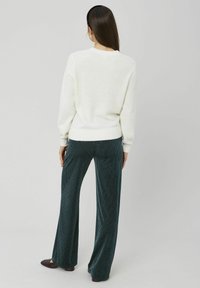 Pull-over en maille crème avec ourlet côtelé, associé à un pantalon large en velours côtelé bleu sarcelle avec des rayures verticales. Design simple, texture douce.