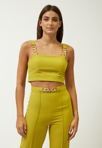 Top corto de color verde lima con tirantes anchos y detalles de cadenas doradas, combinado con pantalones de tiro alto que tienen un cinturón de cadena a juego.