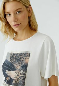 Witte T-shirt met korte mouwen, voorzien van een gedrukt ontwerp met een textuur en kralenaccent rondom een fotografisch patroon. Eenvoudige, relaxte pasvorm.