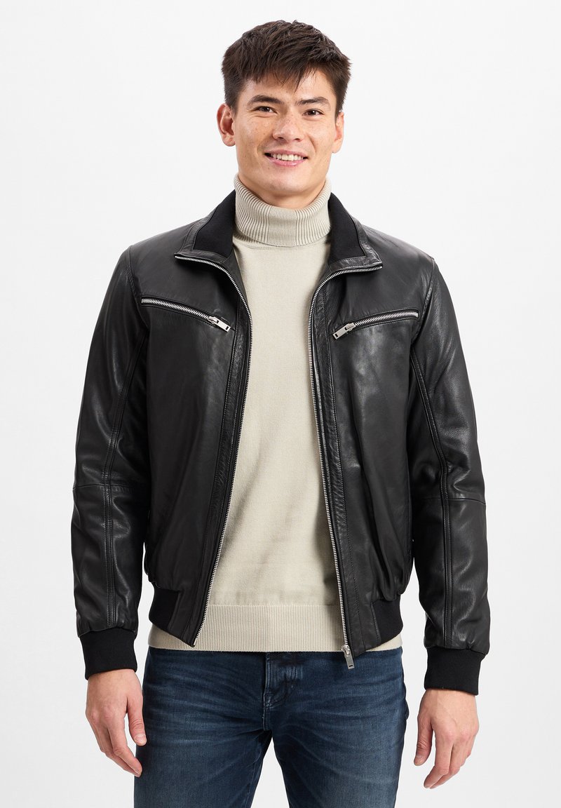 Zwarte leren bomberjack met twee ritssluitingen op de borst, een geribbelde kraag en manchetten, gecombineerd met een lichtbeige coltrui.