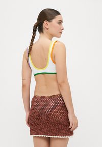 Top bikini bianco in crochet con spalline multicolori; gonna in crochet marrone con motivo triangolare e orlo bianco a zig zag.