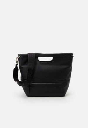 Bolso tote de cuero negro con asas recortadas, bolsillo frontal con cremallera y correa de hombro ajustable sobre un fondo liso.