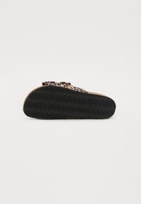 Zwarte rubberen zool met golfpatroon, met een bovenkant in beige en donkerbruin met een luipaardprint. Inclusief een strikaccent op de band.
