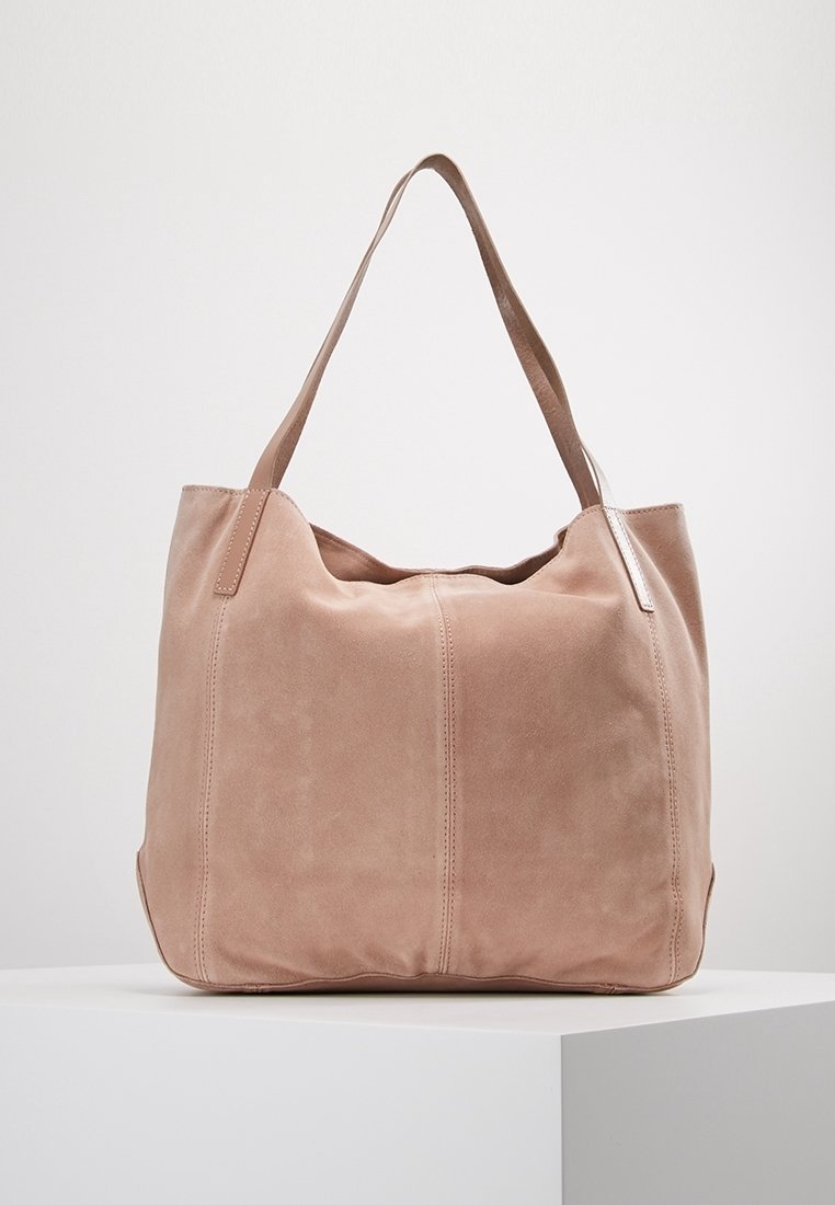 Sac fourre-tout en daim rose doux avec deux longues bandoulières, comprenant un compartiment principal et des détails de couture discrets sur le devant.