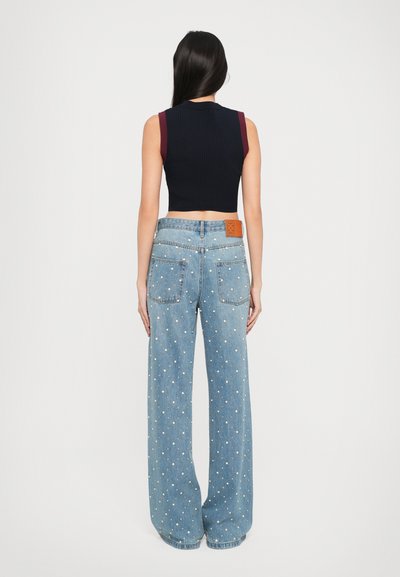 Čierny rebrovaný crop top s marhuľovými ramennými akcentmi, spárovaný s svetlomodrými širokými nohavicami s bielymi bodkami a hnedou koženou visačkou.