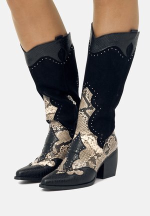 Botas de vaquero de ante negro con un patrón de piel de serpiente, punta afilada, tachuelas decorativas y una parte superior de cuero negro texturizado. Diseño de tacón bloque.