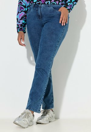 Blaue Jeans aus Denim mit geradem Bein, mittlerer Taille und minimalen Ziernähten, kombiniert mit hellgrauen Turnschuhen.