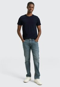 Granatowy bawełniany t-shirt z krótkim rękawem, zestawiony z jasnoniebieskimi dżinsami i białymi tenisówkami; luźny krój z prostym wzorem.