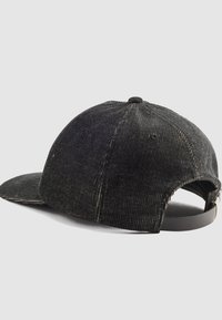 Gorra de pana negra con visera curvada, tejido texturizado y correa trasera ajustable. Cuenta con seis agujeros de ventilación y un botón superior cosido.