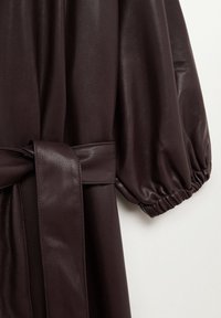 Prenda de cuero marrón oscuro con cintura ceñida por un cinturón, mangas abullonadas con puños elásticos y una textura suave y brillante.