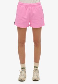 Roze katoenen shorts met een elastische tailleband, voorzien van een rafelige zoom en een klein merkimpressie aan de zijkant. G gedragen met sneakers in neutrale tinten.