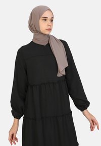 Musta tiered dress dengan lengan panjang, aksen berkerut, dan tekstur yang halus. Dipadukan dengan hijab coklat muda.