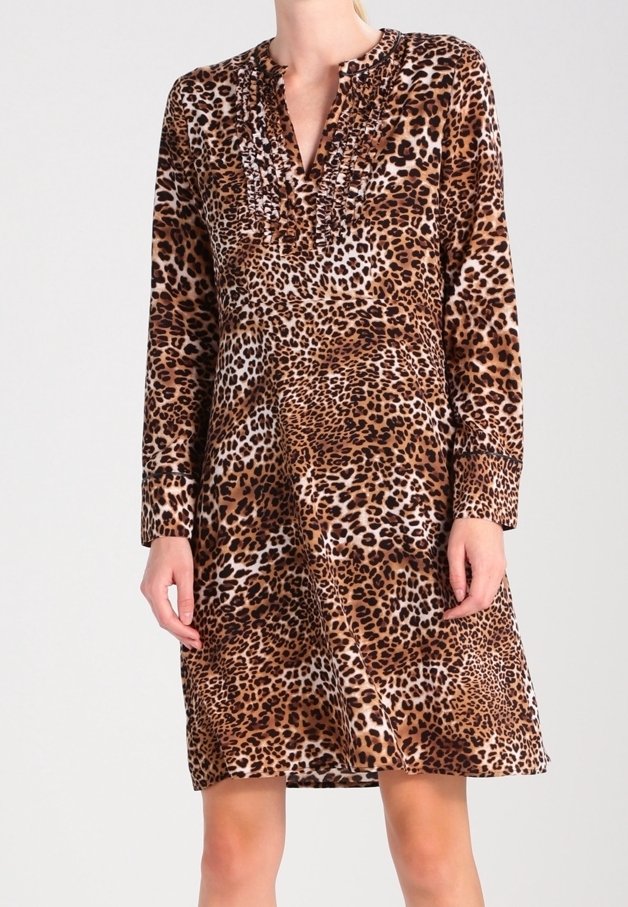 Femme portant une robe imprimé léopard à manches longues et longueur genou avec un col en V à volants, debout devant un fond uni.