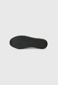 Black rubber sole with textured grip pattern, featuring a rounded shape and white edges. Brand name "Converse" printed on the side.