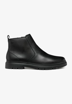Bota de cuero negro hasta el tobillo con cremallera lateral, tira para tirar en el talón y suela gruesa de goma con patrón de tracción para agarre.