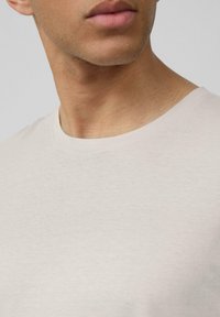 Lichtbeige t-shirt met ronde hals, van een gladde stof en met korte mouwen, voorzien van een subtiele gemêleerde patroon en een klassieke pasvorm.