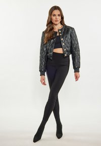 Giacca bomber trapuntata nera con bottoni dorati, indossata sopra un crop top nero e leggings a vita alta, abbinata a stivaletti neri con punta.