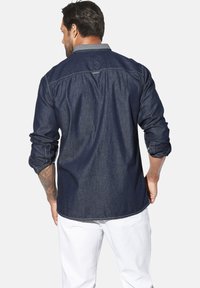 Jeanshemd, dunkelblau, mit hochgerollten langen Ärmeln, Kontrastnähten, Hemdkragen, hinterer yoke Naht, getragen mit weißen Hosen.