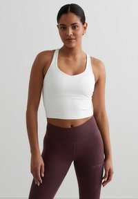 White cropped sports bra with a V-neck design, paired with burgundy high-waisted leggings featuring logo detail and smooth texture.
