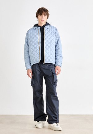 Chaqueta acolchada de color azul claro con cierre frontal, sudadera con capucha de color azul oscuro debajo y pantalones cargo en color azul marino. Zapatillas blancas completan el atuendo.