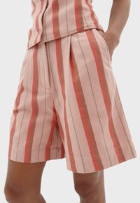 Roze gestreepte shorts met horizontale rode en groene lijnen, voorzien van plooien en zakken, gemaakt van geweven stof met een gestructureerde afwerking.