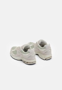 Pár světle béžových a krémových běžeckých bot s detaily z mesh a semiše, tlustými polstrovanými podrážkami a logem značky na stranách a patách.