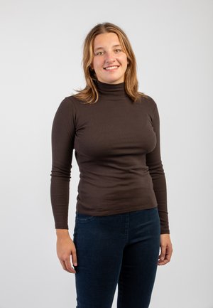 Maglione a collo alto marrone dal design aderente, realizzato in tessuto morbido. Abbinato a jeans in denim scuro, il modello si trova di fronte a uno sfondo neutro.