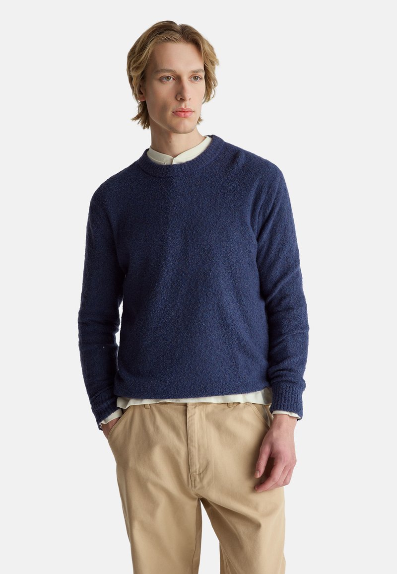 Marineblauer, strukturierter Pullover mit Rundhalsausschnitt und langen Ärmeln, kombiniert mit hellbeigen Hosen. Gerippte Bündchen und Saumdetails.