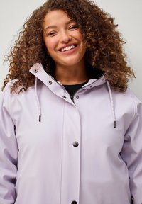 Giacca impermeabile lavanda chiaro con zip frontale, bottoni a pressione, cappuccio regolabile con lacci e texture liscia.