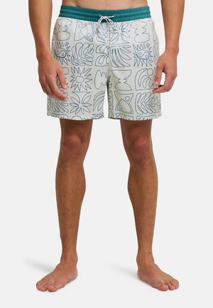 Short de bain homme avec taille élastique bleue et motifs abstraits en lignes bleu foncé sur tissu blanc, porté pieds nus.