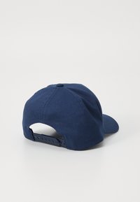 Tamsiai mėlyna medvilninė kepurė su išlenktu kraštu, reguliuojamu snapback užsegimu ir lygiu paviršiumi. Galinis vaizdas, akcentuojantis dirželį.