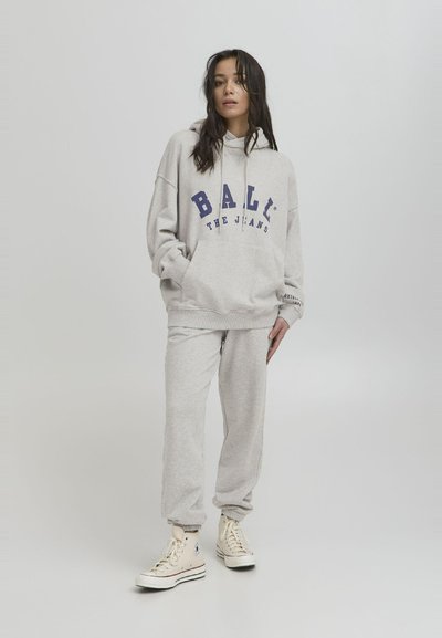 Grå hettegenser med "BALI THE JEANS" trykket i blått, kombinert med matchende grå joggebukser og beige høye sneakers. Myk stoff, avslappet passform.