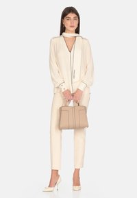Blusa crema con rifiniture nere, abbinata a pantaloni crema su misura. Borsa strutturata beige e scarpe con tacco avorio con decorazioni.