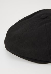 Black wool flat cap with a rounded shape. Features a small, round top button and subtle stitching details along the seams. Soft texture.