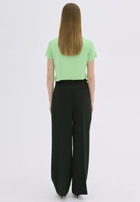 Un top verde cu mâneci scurte, combinat cu o pereche de pantaloni negri, cu talie înaltă și croi larg. Material neted cu o siluetă elegantă. Fără modele sau detalii vizibile.