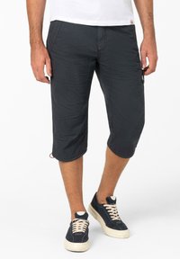 Schwarze knielange Cargo-Shorts mit strukturierter Oberfläche, ausgestattet mit Seitentaschen und gesteppten Akzenten, kombiniert mit dunklen Sneakern.