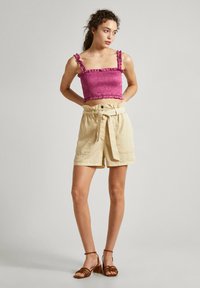 Top corto fruncido fucsia con tirantes rizados, combinado con pantalones cortos beige con cinturón y tacones marrones con tiras. Tejido simple y texturizado con formas definidas.