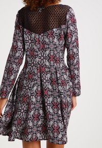 Abito nero con maniche lunghe, intricato motivo floreale rosso e bianco e dettaglio in pizzo sul collo. La gonna svasata esalta il design.