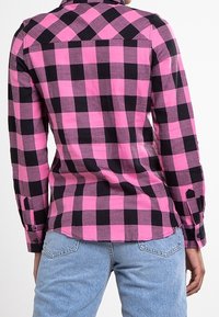 Checkered shirt in pink and black fabric, featuring long sleeves, a collar, and a front yoke. The back showcases a curved hem and buttoned cuffs.