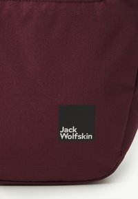Burgundy fabric bag with a smooth texture, featuring a black rectangular logo with white text "Jack Wolfskin" at the bottom right corner.