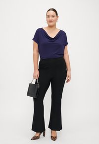 Blusa púrpura con drapeado, pantalones negros de campana, tacones de leopardo marrón, y un pequeño bolso negro con cadena. Texturas suaves en general.