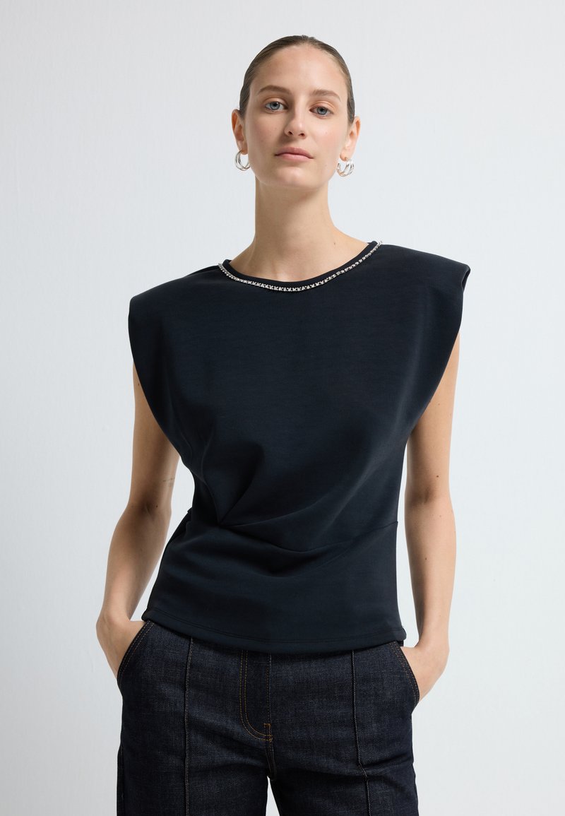 Top senza maniche nero con scollatura rotonda, caratterizzato da un dettaglio con perline. Tessuto morbido, forma scultorea e sottile drappeggio.