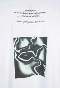 "Prostota jest chwałą wyrazu..." nad abstrakcyjnym czarno-białym płynącym wzorem na białym tle tkaniny.