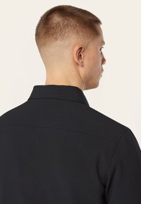 Zwarte shirt met een klassieke kraag, gezien van achteren. Kenmerkt zich door gladde stof, gestructureerde pasvorm en een minimalistisch ontwerp zonder versieringen.