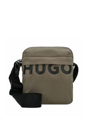 Piccola borsa a tracolla verde oliva con tracolla nera regolabile e grande scritta parziale "HUGO" sul davanti.