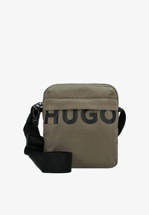 Kleine olijfgroene crossbodytas met zwarte verstelbare band en grote gedeeltelijke "HUGO" tekst aan de voorkant.