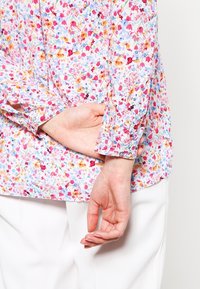 Mønstret blomsterbluse i flere farver med let stof, rund halsudskæring, knaplukning foran og lange ærmer med knapmanchetter.
