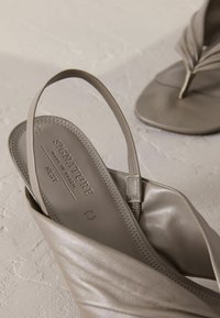Leather sandals in muted gray with a wide toe strap and a thin ankle strap, featuring a textured footbed and subtle stitching details.