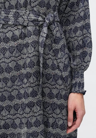 Φόρεμα με μακρύ μανίκι από γκρι ύφασμα με ανθισμένο μοτίβο σε ναυτικό μπλε. Διαθέτει δέσιμο στη μέση και ελαστικές μανσέτες, που αναδεικνύουν το υφασμάτινο σχέδιο.