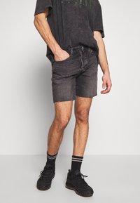 Dark grey denim shorts with frayed hem, paired with an oversized black t-shirt and black sneakers with striped socks.